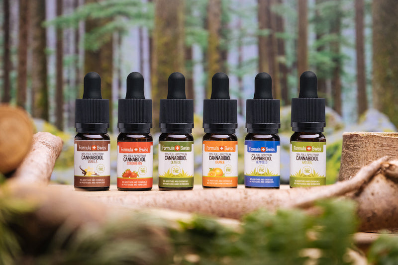Šesť full spectrum CBD olejov Formula Swiss s rôznymi nosnými olejmi a príchuťami pred lesom