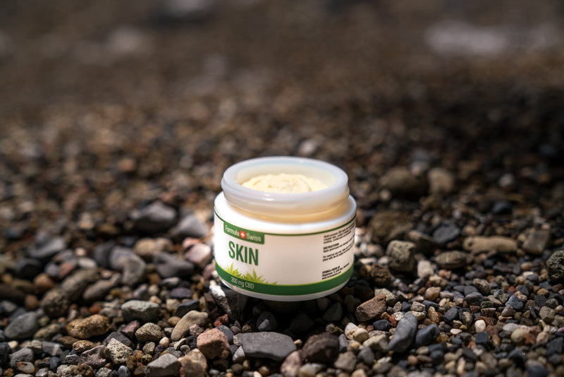 Otvorená dóza balzamu Formula Swiss CBD Skin, 300 mg CBD, na kamienkovej pláži