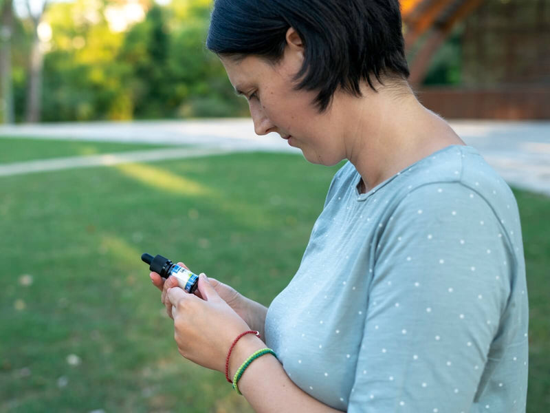 Žena vonku sa pozerá na fľaštičku CBD oleja Formula Swiss vo svojej ruke